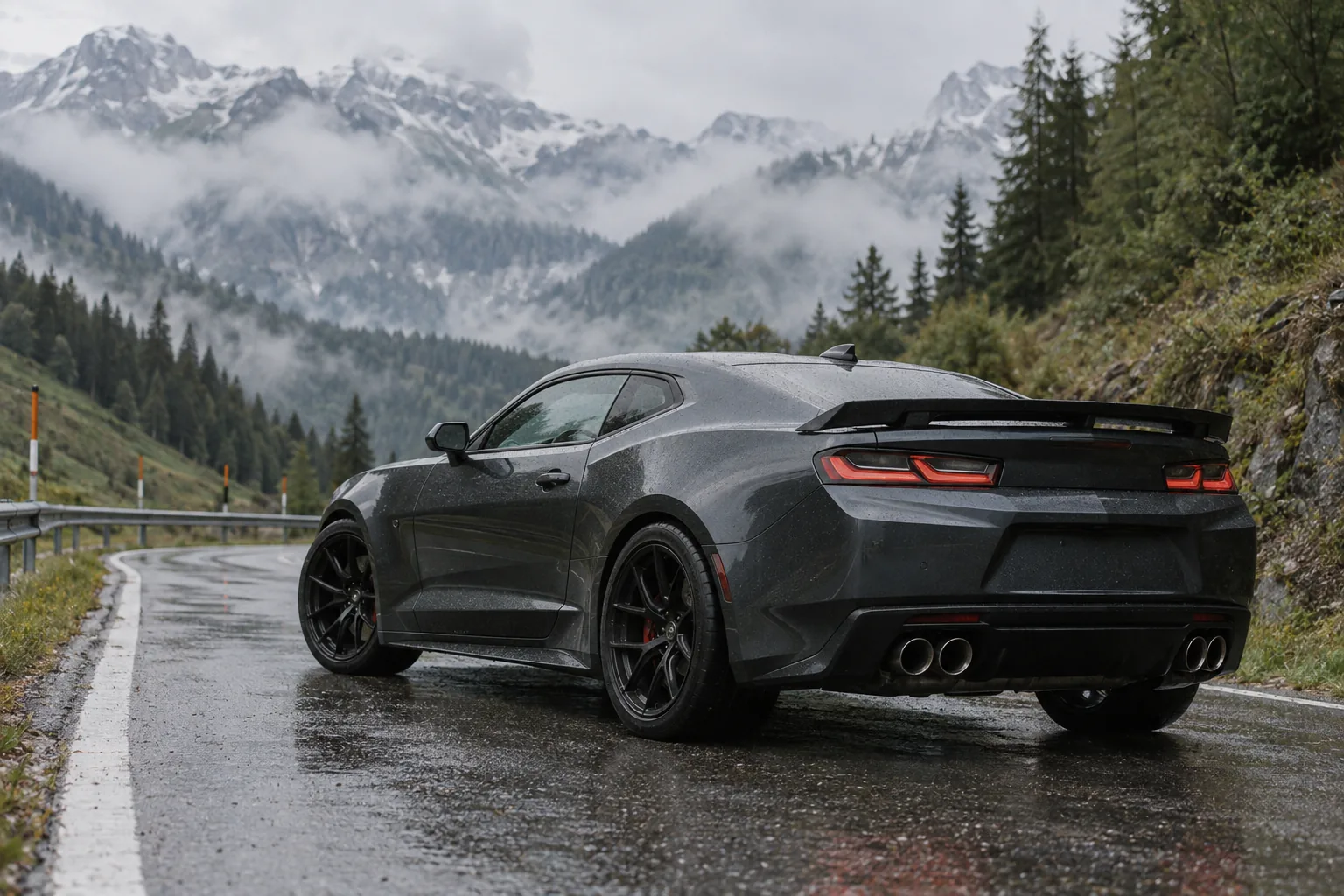 Dunkelgrauer Chevrolet Camaro SS 1LE der sechsten Generation von hinten auf einer nassen Passstraße in den Alpen